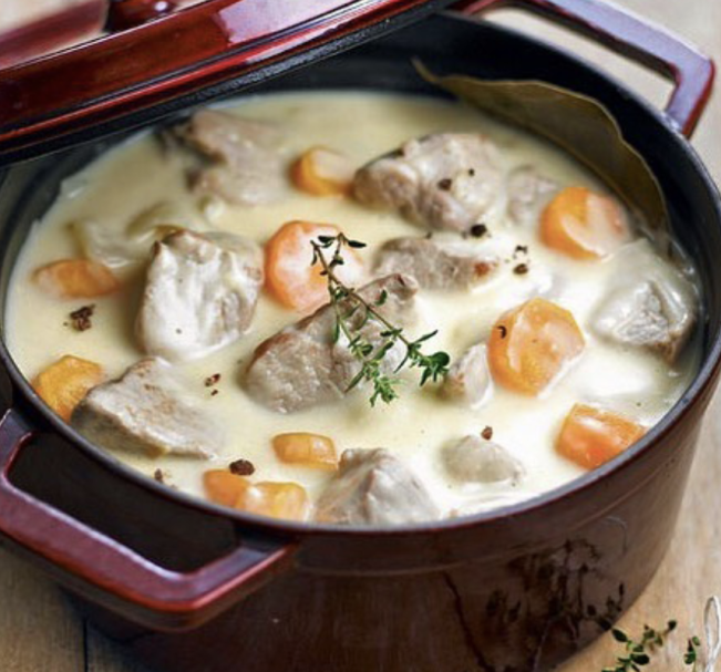 Blanquette de veau blanquette de beau présentée dans une cocotte en fonte de couleur bordeaux: morceaux de viande, rondelles de carotte et brin de thym
