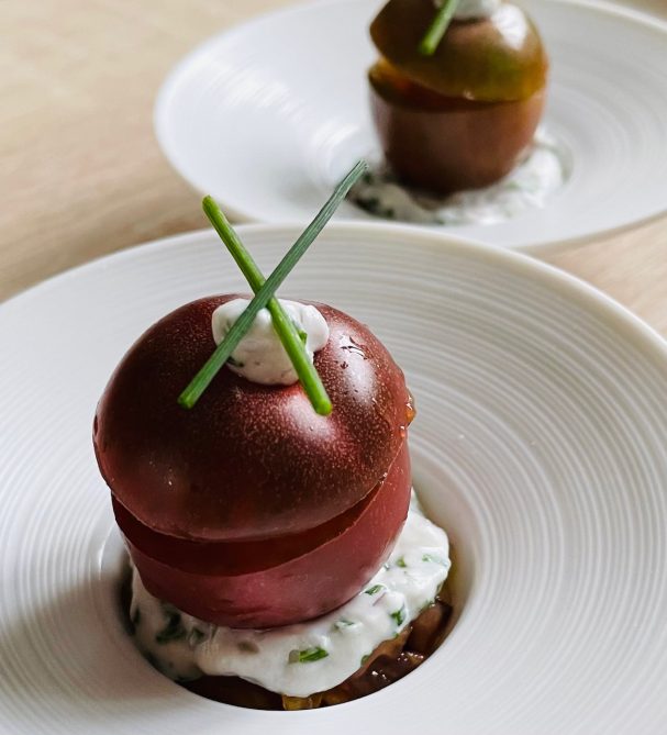 Tomte cerise en mise en bouche assiette creuse blanche tomate cerise posée sur un lit de lentilles vertes recouvert d'un fromage blanc de chèvre aux herbes