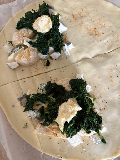 les 4 étapes 2 demi rond de pâte feuilletée sur feuille avec des épinards cuits, fromage de chèvre en morceaux, herbes sel et poivre
